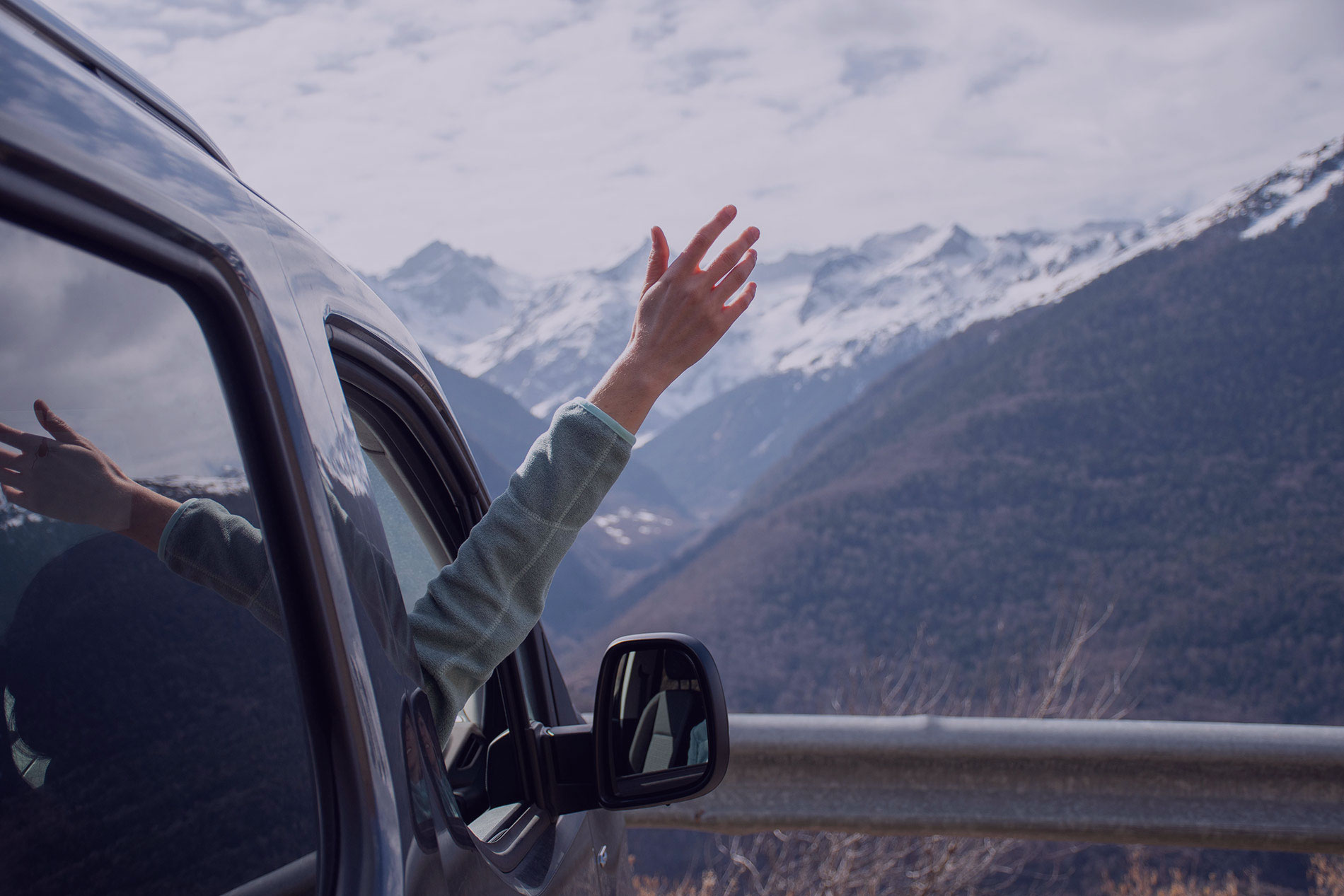 Hand raised out of a car window at a mountain viewpoint